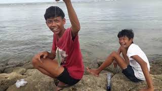 Senang Sambil Tunjukan Ikan Hasil Mancing Di Atas Batu Karang Penangkal Ombak Tepi Pantai Sindu.